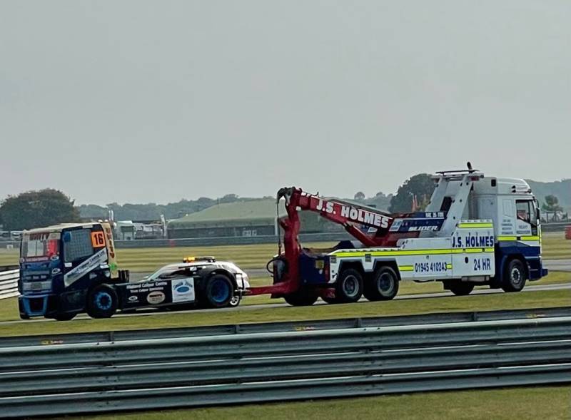 J.S. Holmes recovery truck towing a racing car on a race track. The racing car is black and blue with the number 16 on the side