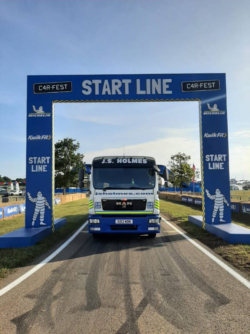 J.S. Holmes recovery truck driving through a start line archway at a race event.