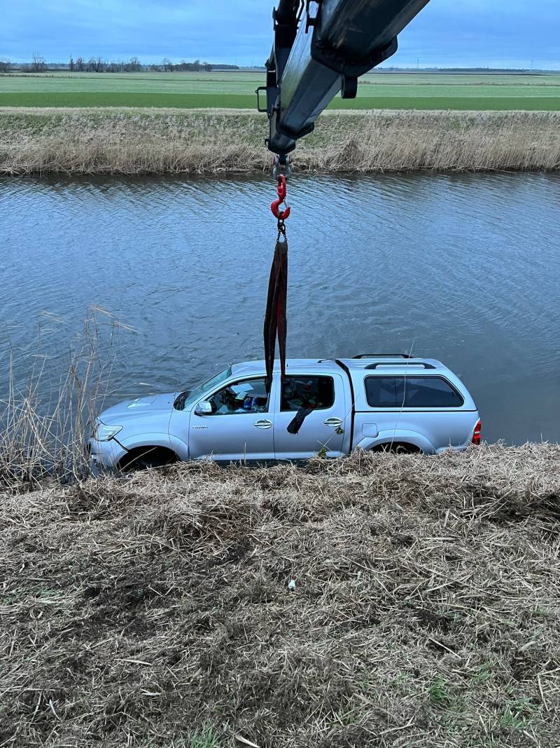  JS Holmes recovery truck using a crane to lift a pickup truck out of a canal. 