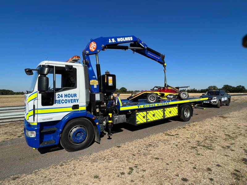 J.S. Holmes recovery truck lifting a small racing car onto its trailer. 
