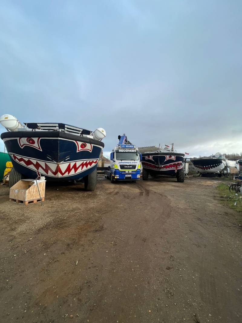 three large amphibious vehicles parked in a row. The central vehicle is a J.S. Holmes recovery truck, its crane arm extended 